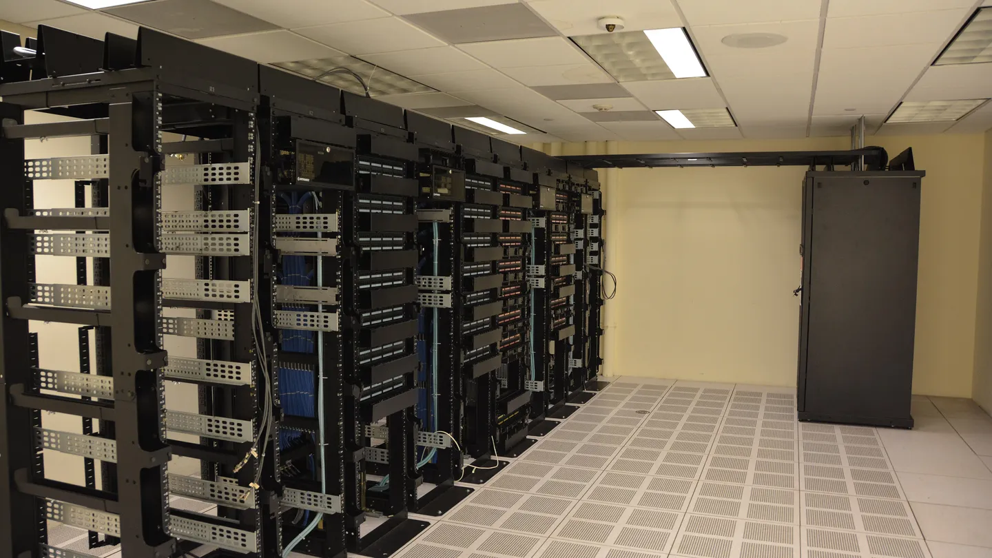 Rows of black server racks in a data center with a tiled floor